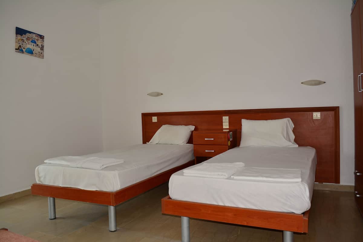 A room with two single beds, wooden headboards, white bedding, and a small wooden nightstand with a drawer.