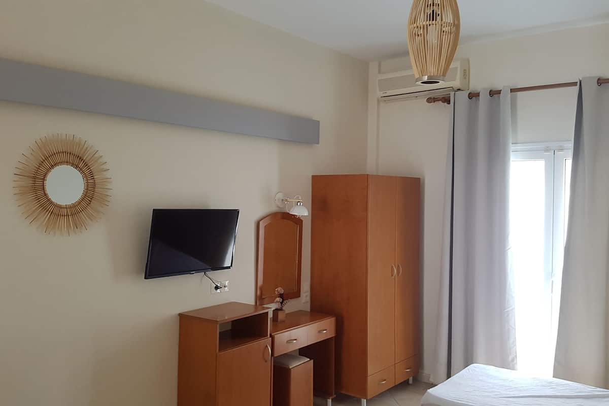 A bedroom with a bed, a TV, a wardrobe, a desk, a mirror, and a sunburst wall decoration.