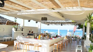 An outdoor bar area with a white counter, wooden stools, and a view of the sea. - Cavo D'Oro Apartments (Corfu)