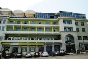 A multi-story building with a bank, a hotel, and several parked cars. - Cajupi (Gjirokastër)