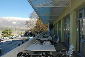 An outdoor seating area with tables and chairs, overlooking a street and mountains. - Cajupi (Gjirokastër)