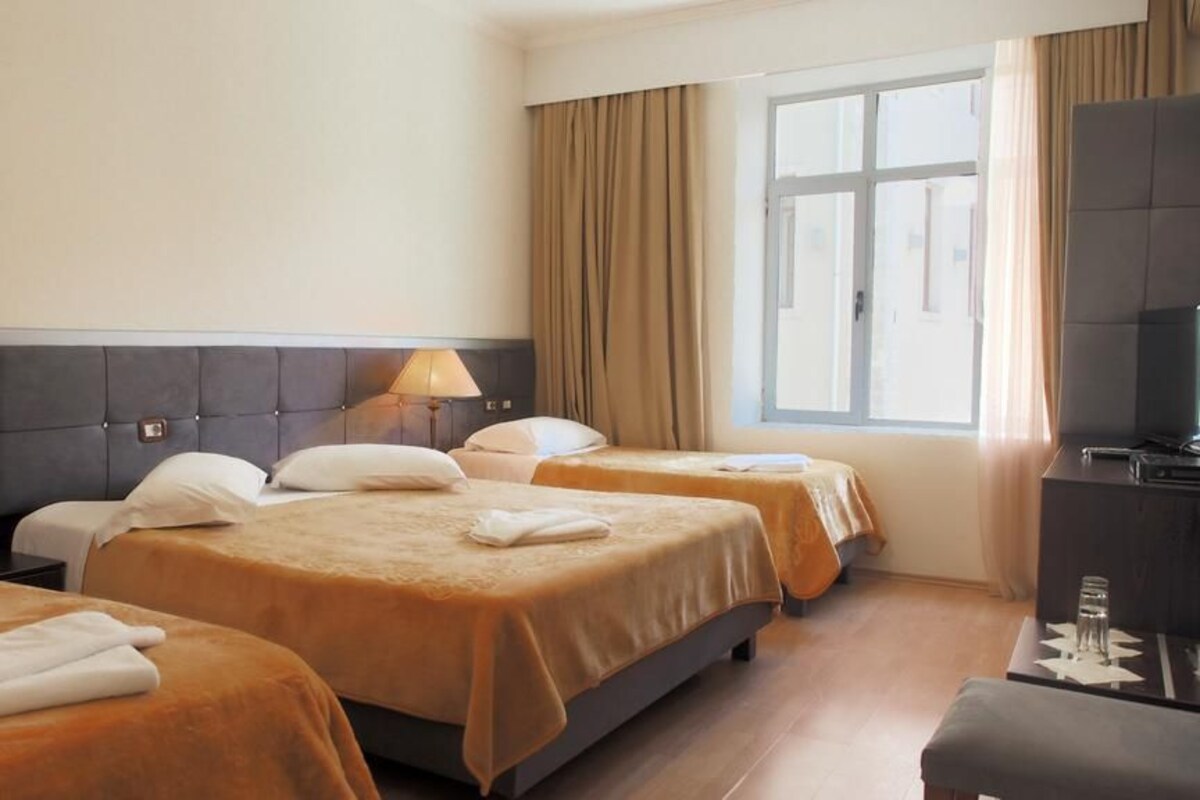 Ein Hotelzimmer mit zwei Betten, einem Schreibtisch, einem Fernseher und einem Vorhangfenster.