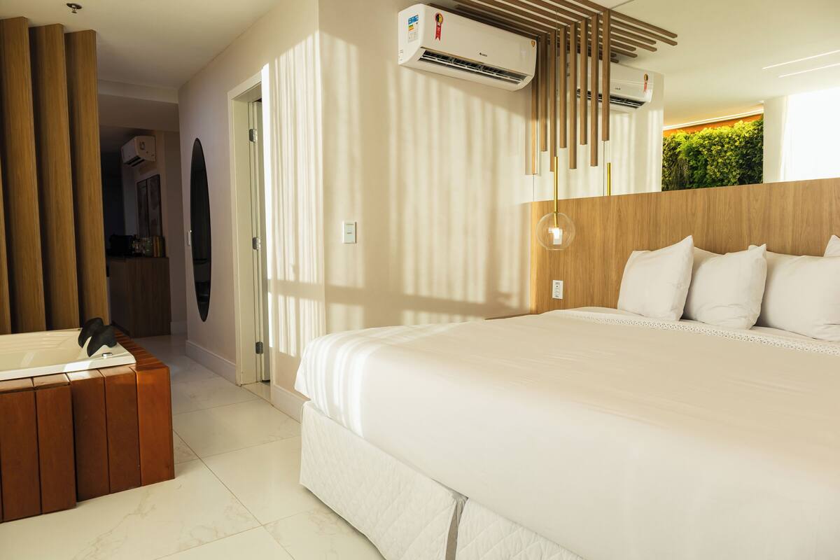Habitación de hotel con una cama grande, una mesita de noche de madera, un equipo de aire acondicionado y un adorno verde en la pared.