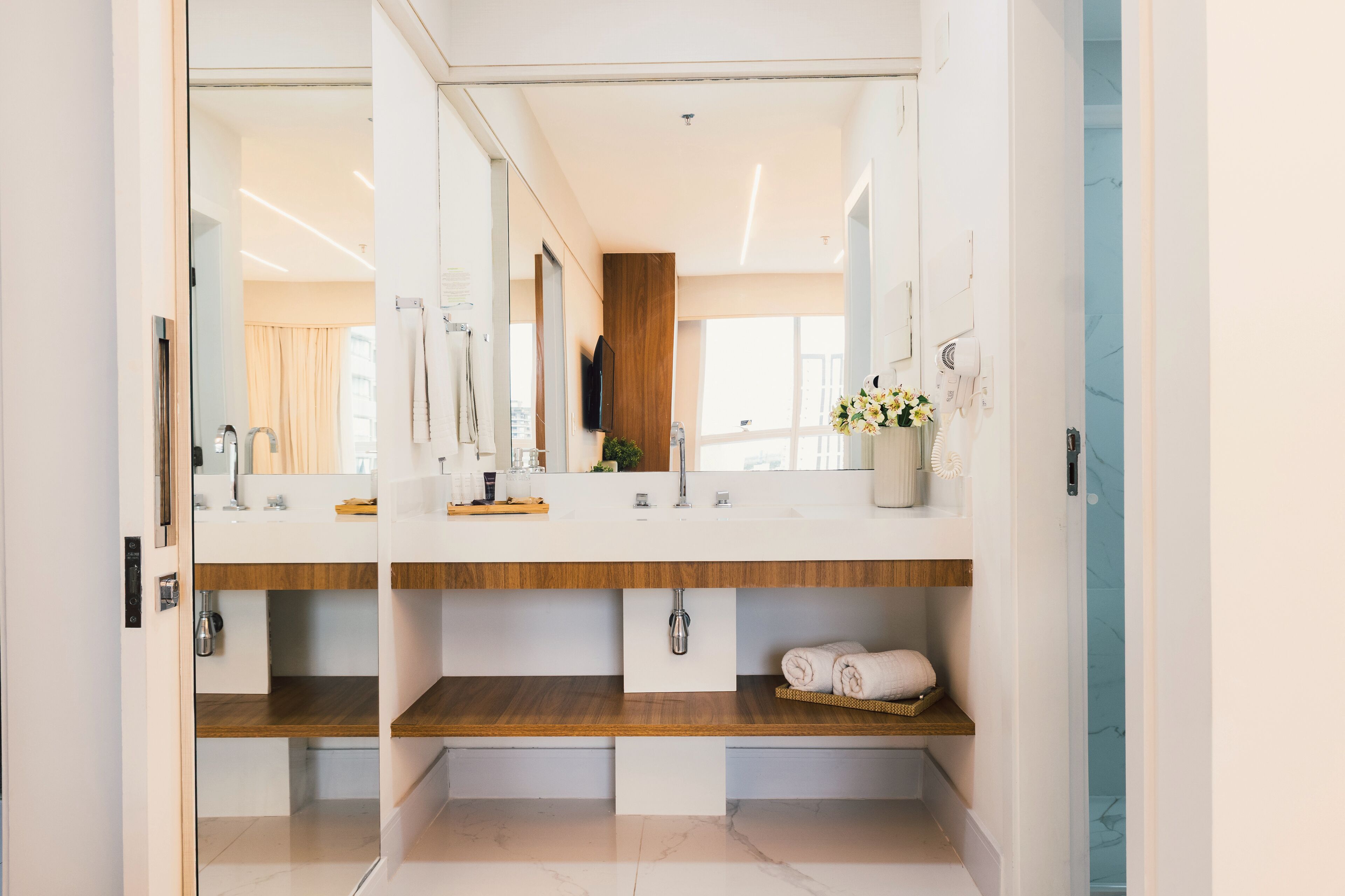 Une salle de bain moderne avec deux vasques, des étagères en bois, un miroir et un porte-serviettes.