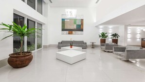 Un vestíbulo moderno y espacioso con una planta en maceta grande, una mesa de centro blanca y un sofá gris.