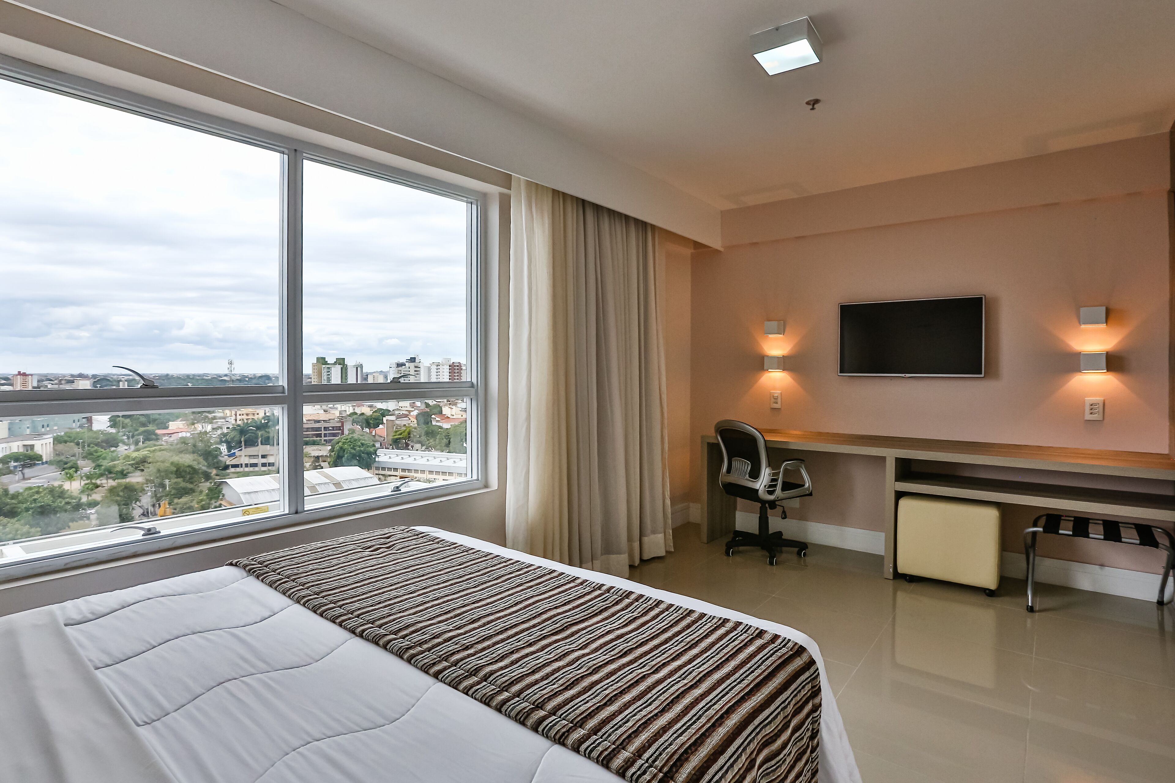 Une chambre d’hôtel avec un grand lit, un bureau, une chaise, une télévision et une vue sur le paysage urbain par la fenêtre.