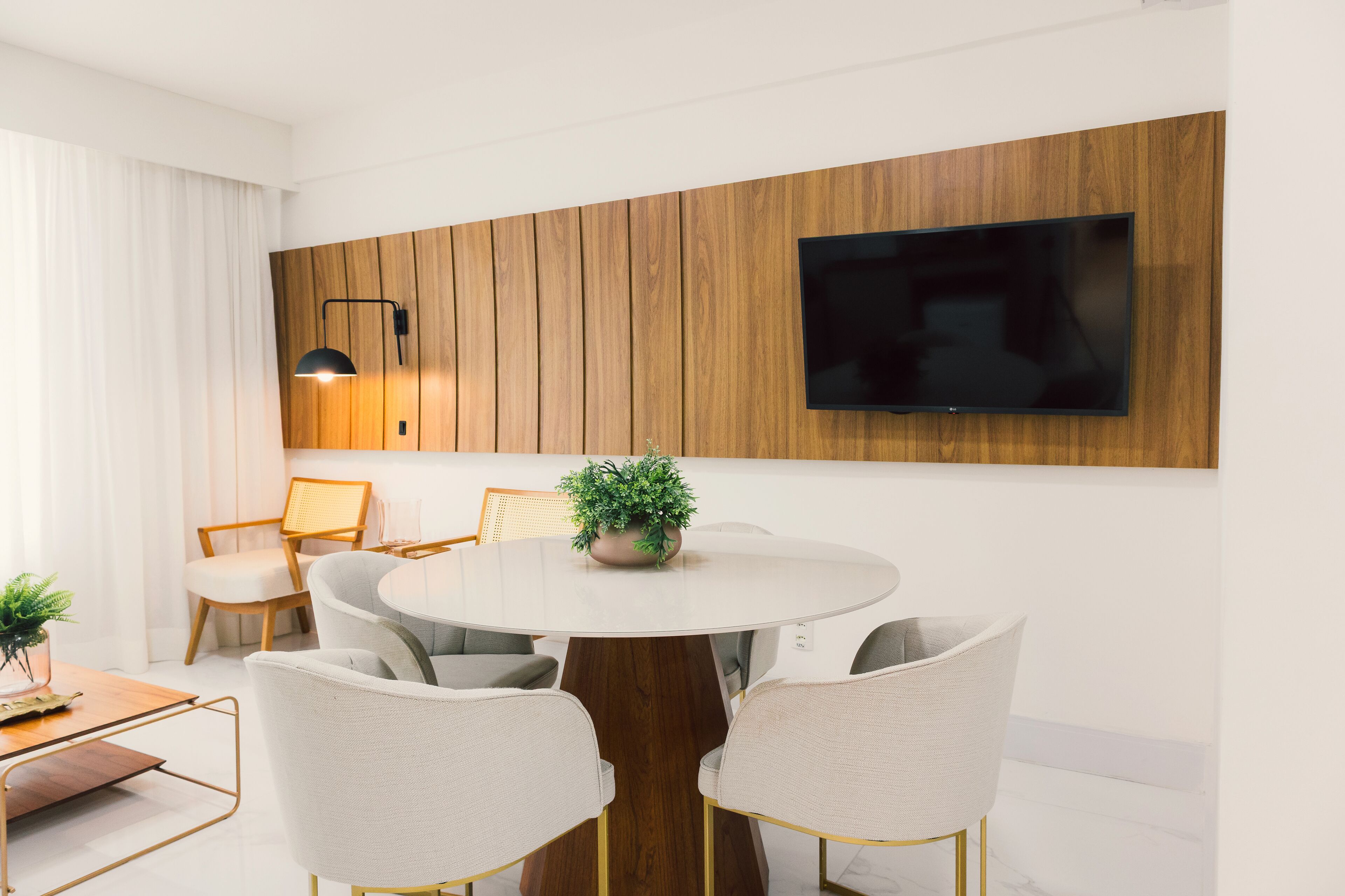 Un comedor moderno con una mesa redonda, cuatro sillas, una planta en maceta y un televisor montado.