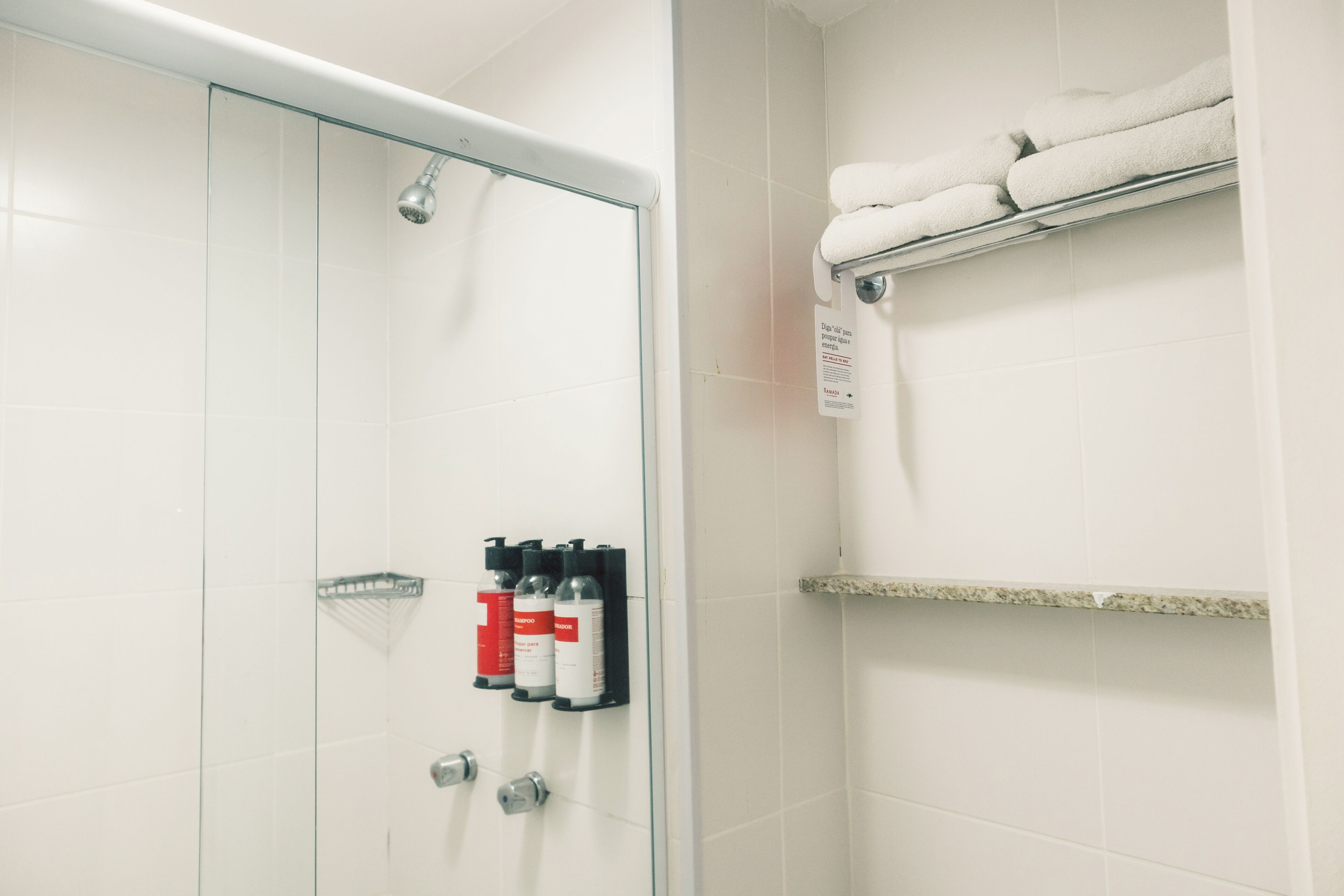 A modern bathroom with a glass shower door, white tiles, and a towel rack with neatly folded towels.