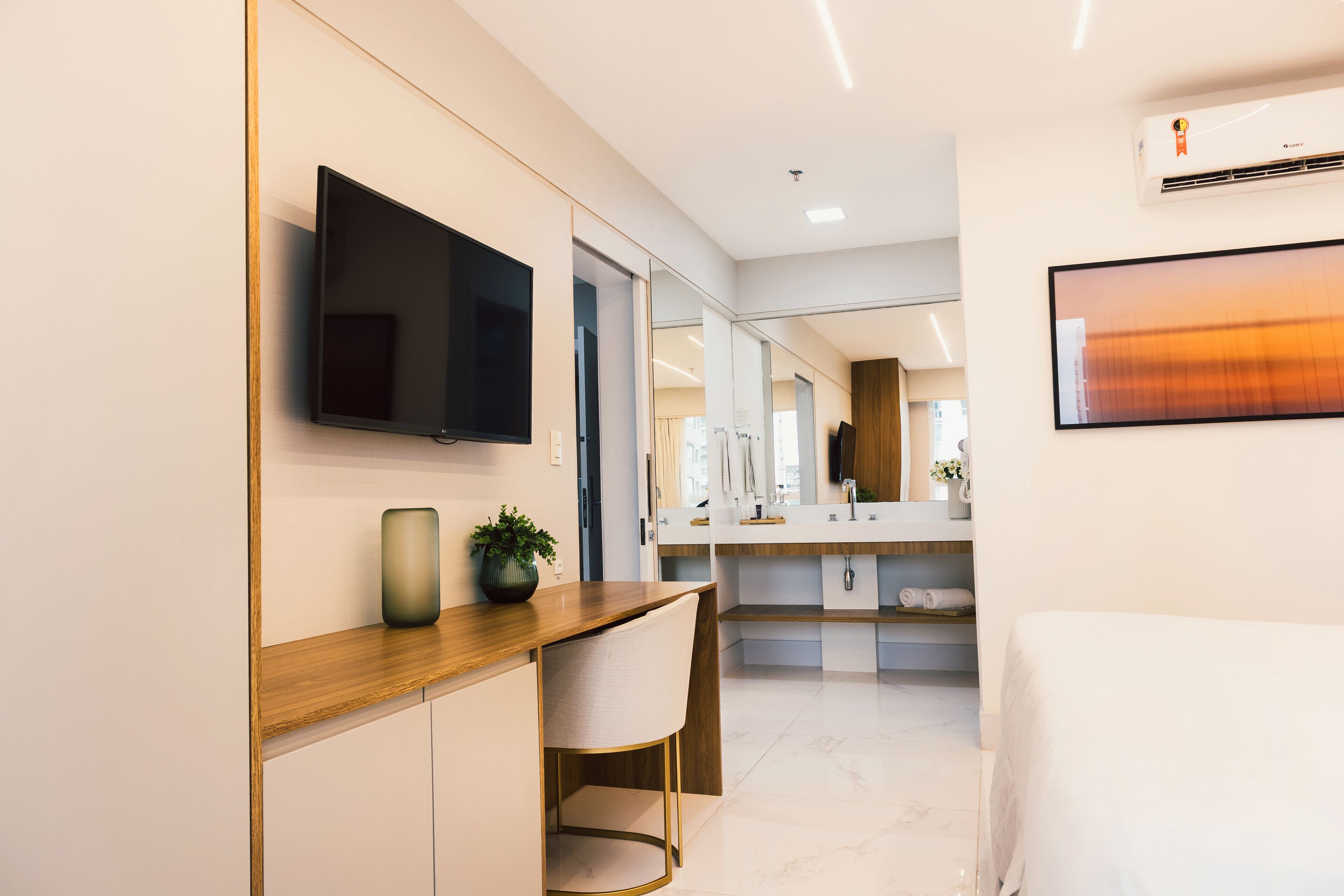 Une chambre d’hôtel moderne avec un bureau en bois, un téléviseur à écran plat, un grand miroir et un lit.