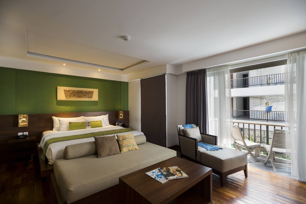 A hotel room with a bed, a sofa, a coffee table, a chair, and a balcony with a railing.