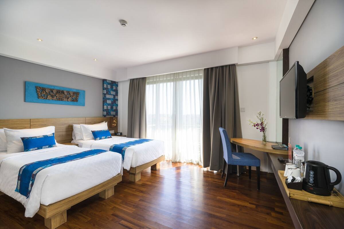 A hotel room with two beds, a desk, a chair, a TV, and a coffee maker.