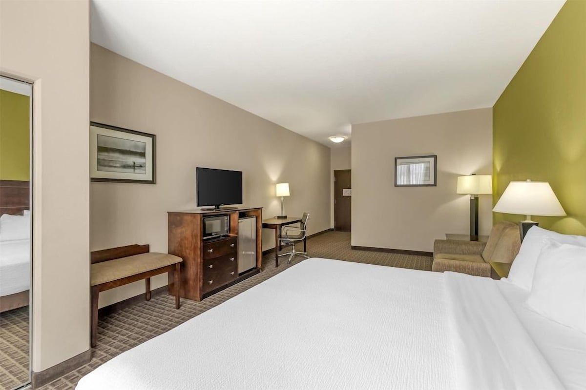 A hotel room with a large bed, a desk with a chair, a television, and two lamps.