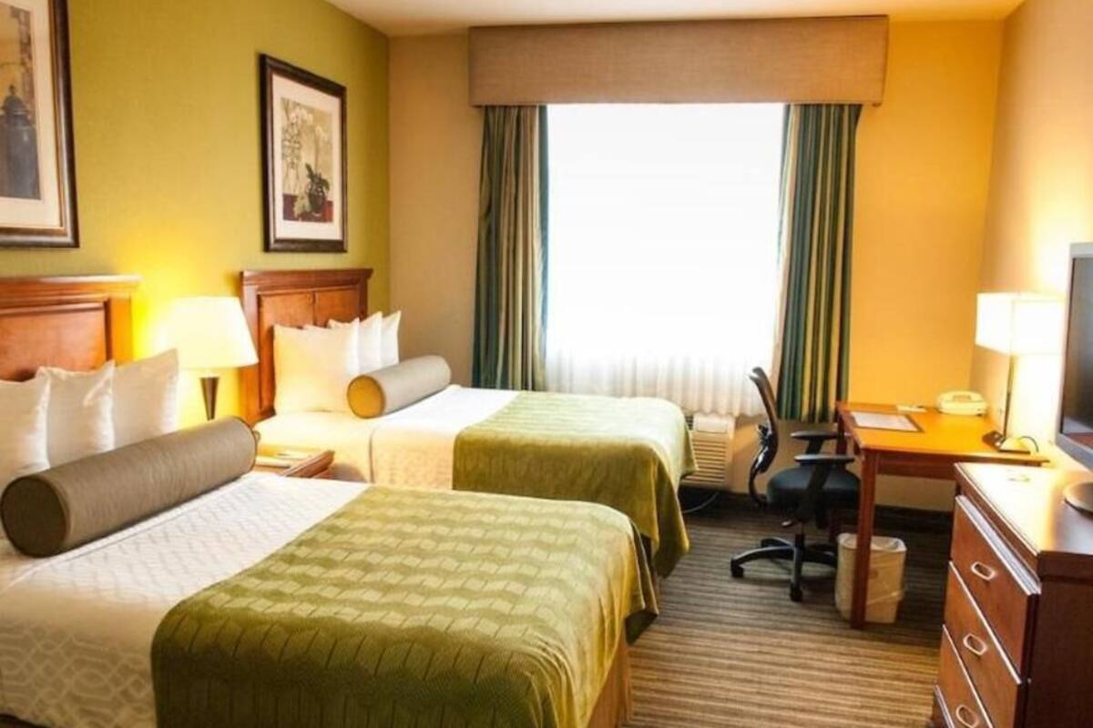 Habitación de hotel con dos camas, un escritorio, una silla, una cómoda y una ventana con cortinas.