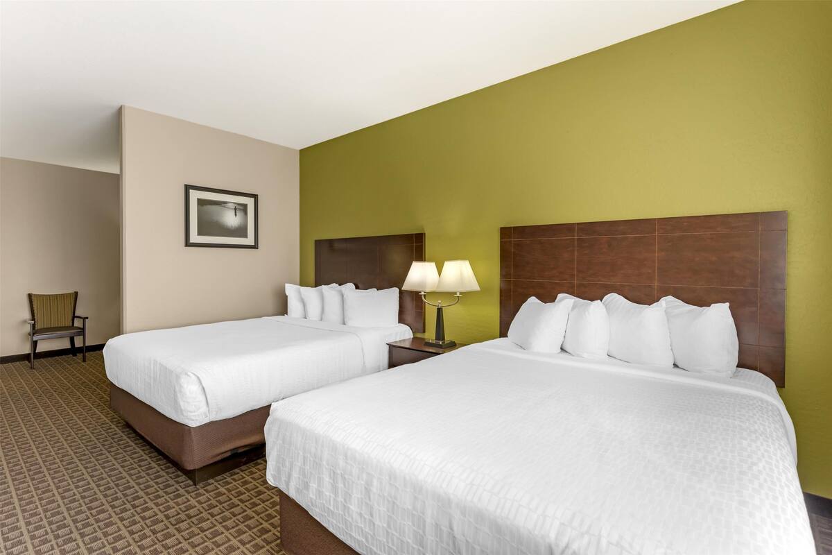 Habitación de hotel con dos camas, una silla, una lámpara y un cuadro en la pared.