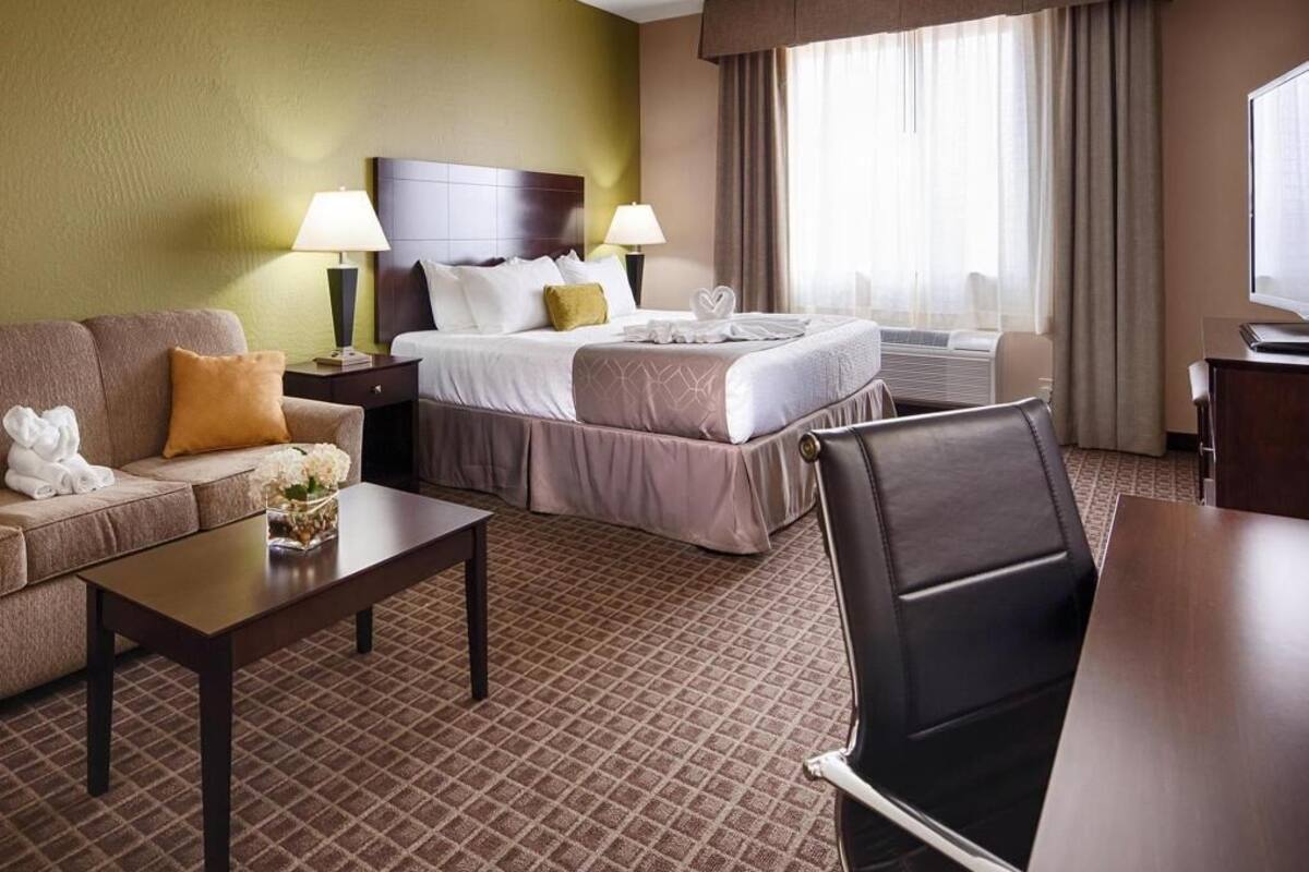 Una habitación de hotel con cama, sofá, mesa de centro, escritorio y televisor.