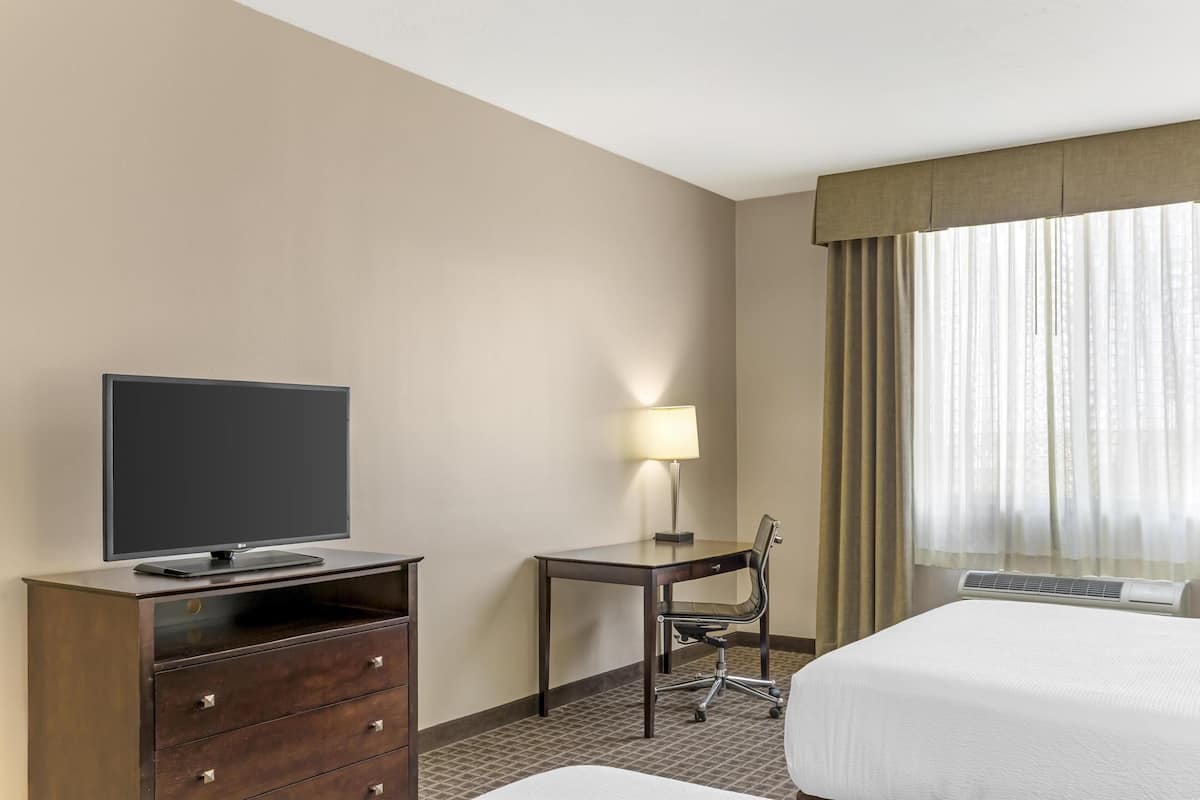 Habitación de hotel con cama, escritorio y silla, televisor en una cómoda y ventana con cortinas.