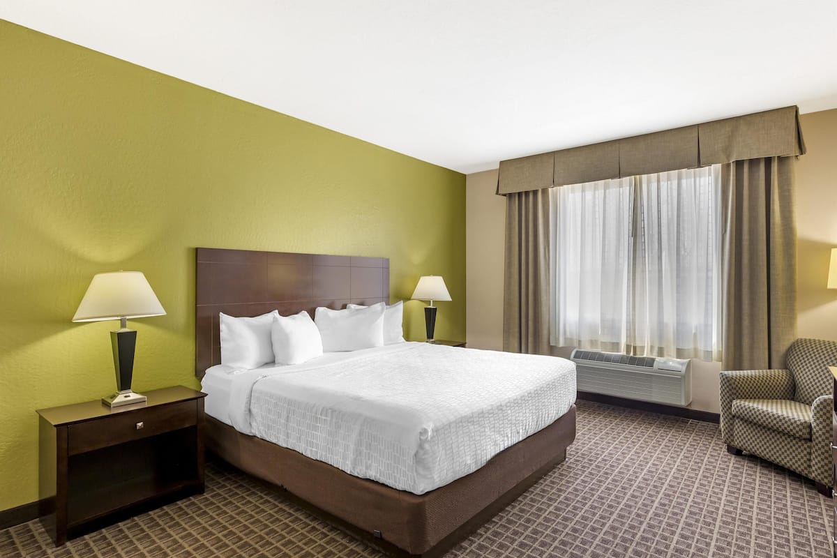 Una habitación de hotel con una cama grande, dos lámparas de noche, una silla y una ventana con cortinas.