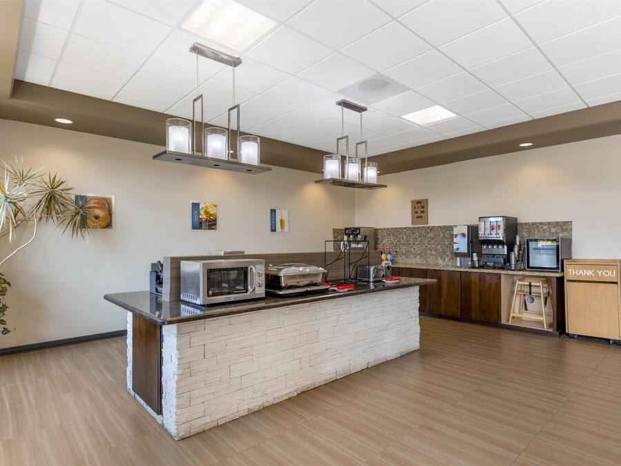 Un área de cocina moderna con una isla central, microondas integrado, tostadora y cafetera. Hay luces colgantes sobre la isla, y un cartel que dice “THANK YOU” a la derecha.