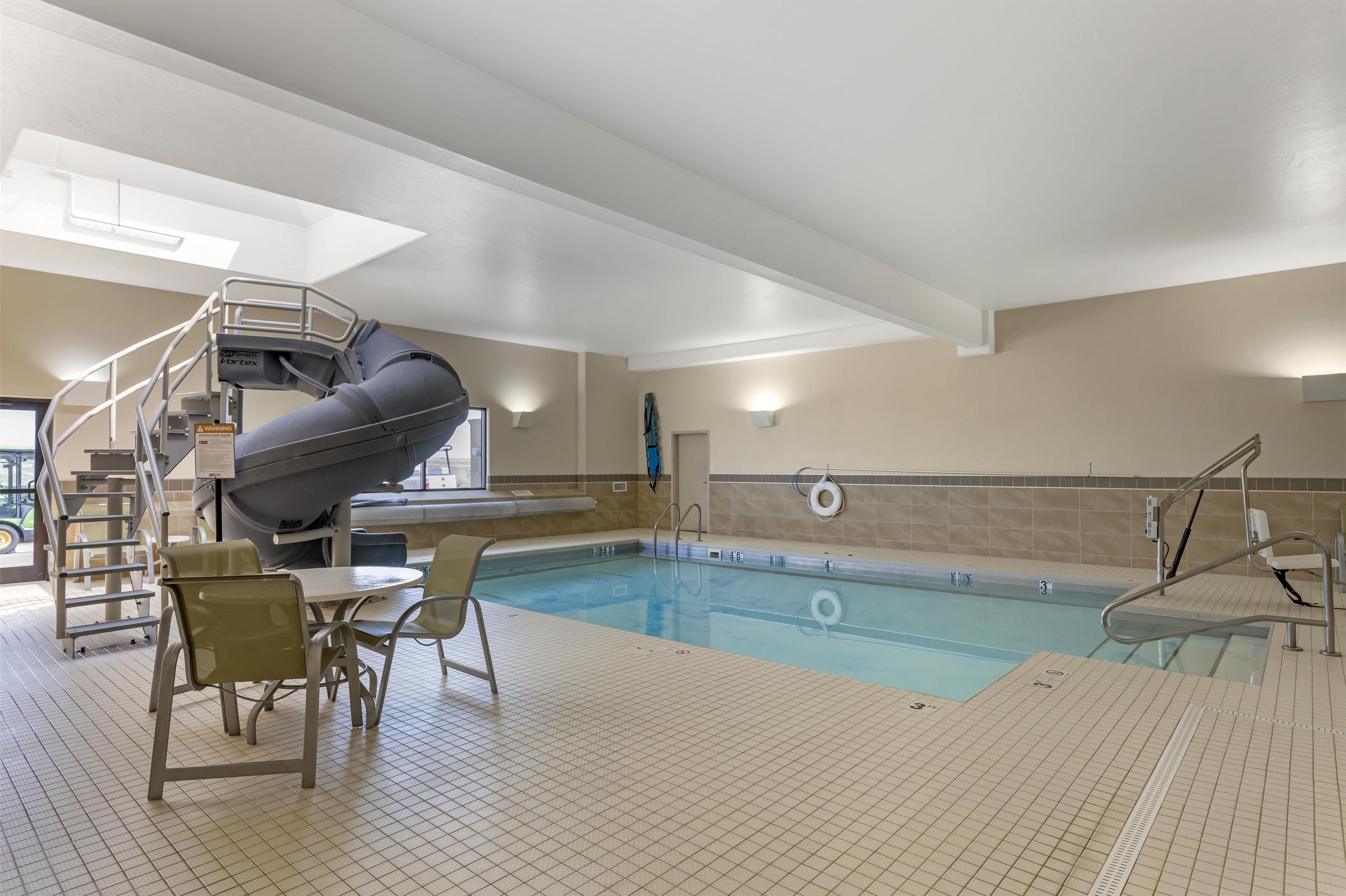 Piscina interior com escorregador, cadeiras e cadeira do salva-vidas.