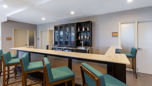 A bar area with a long counter, bar stools, and a cabinet with bottles.