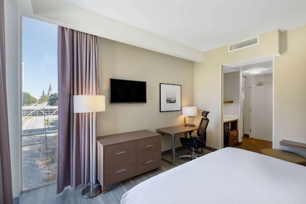A hotel room with a bed, desk, chair, and a large window with curtains.