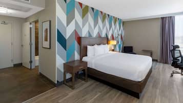 A hotel room with a large bed, a bedside table, a chair, and a colorful geometric wall design.