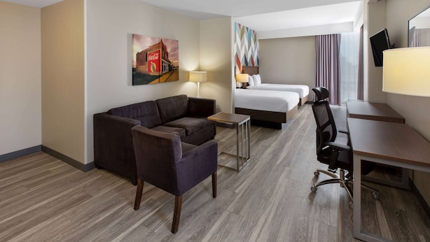 A hotel room with a sofa, a desk, a chair, a bed, and a TV.