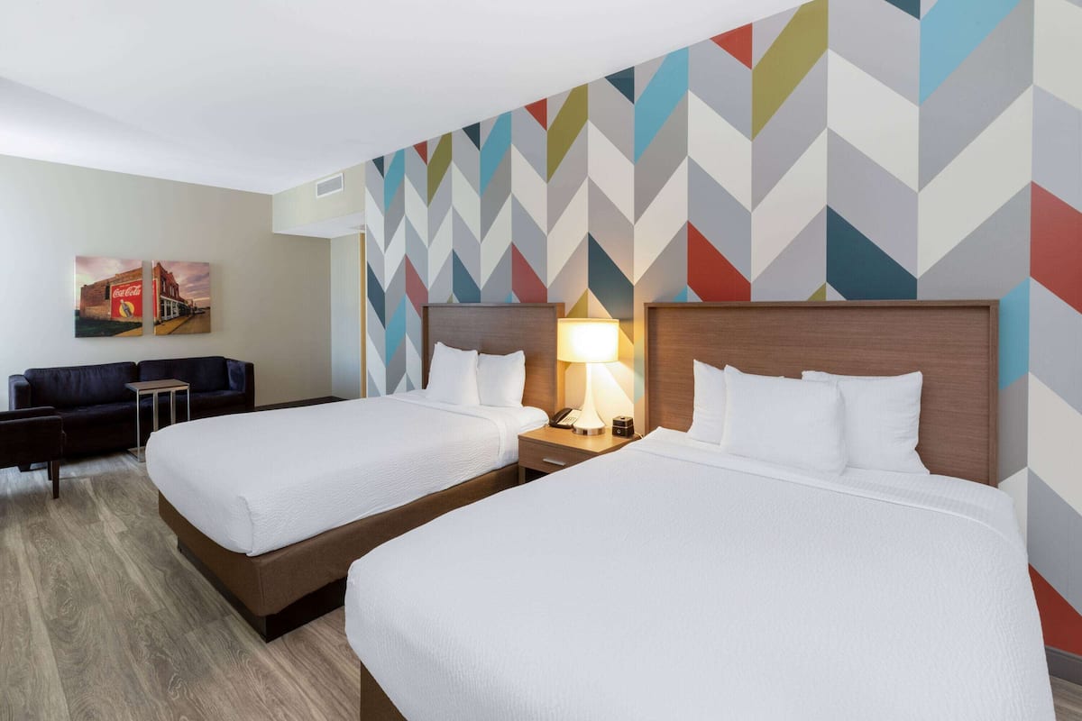 A hotel room with two beds, a sofa, a small table, and a wall with a geometric pattern.