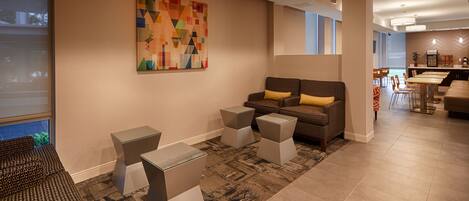 A modern lobby with a sofa, two side tables, a colorful abstract painting, and a dining area with chairs and tables.