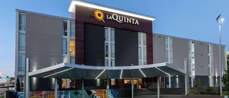 A hotel with a modern design, featuring a prominent 'La Quinta' sign, a covered entrance, and a mural on the side.