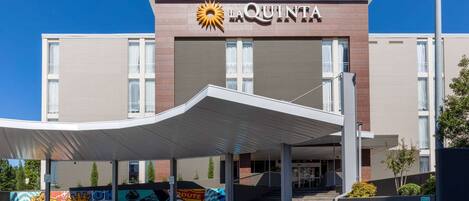 A hotel entrance with a covered walkway, a prominent sun logo, and a mural on the wall.