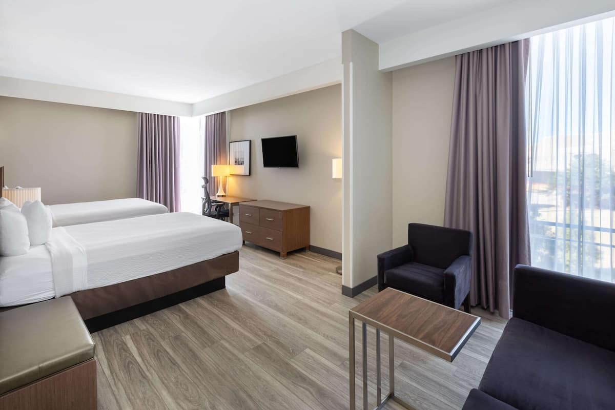 A hotel room with two beds, a desk, a chair, a TV, and a window with curtains.