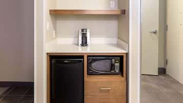 A compact kitchenette with a black refrigerator, a microwave, and a coffee maker on a white countertop.