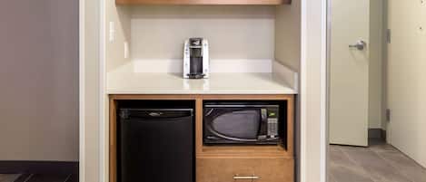 A compact kitchenette with a black refrigerator, a microwave, and a coffee maker on a white countertop.
