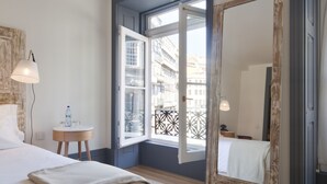 A hotel room with a large bed, a bedside table with a lamp, a small round table with a water bottle, and a large mirror. - Porto A.S. 1829 Hotel (Porto)