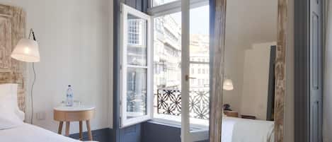 Une chambre d’hôtel avec un grand lit, une table de chevet avec une lampe, une petite table ronde avec une bouteille d’eau et un grand miroir.