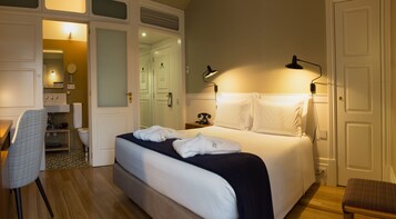 Une chambre d’hôtel comprenant un lit, des lampes de chevet, un bureau, une chaise, un miroir, une salle de bain et un téléphone.
