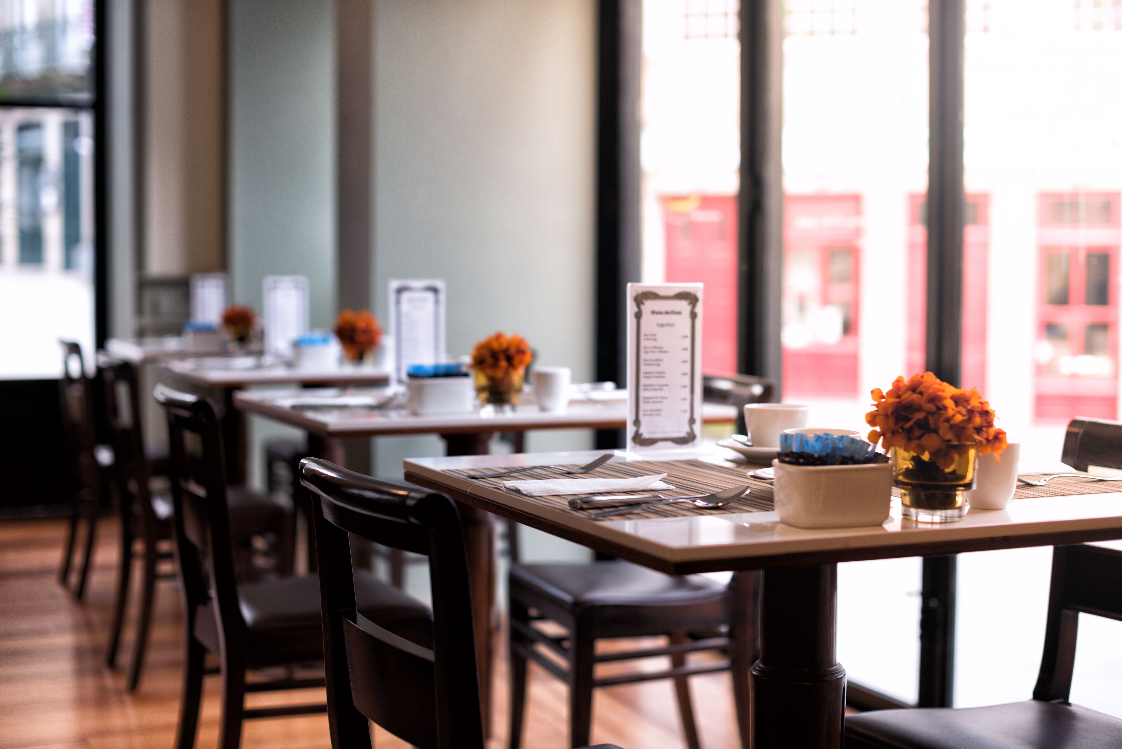 Un restaurant avec des tables et des chaises en bois, des menus et des compositions florales.