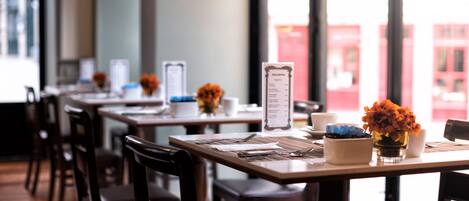 Un restaurant avec des tables et des chaises en bois, des menus et des compositions florales.