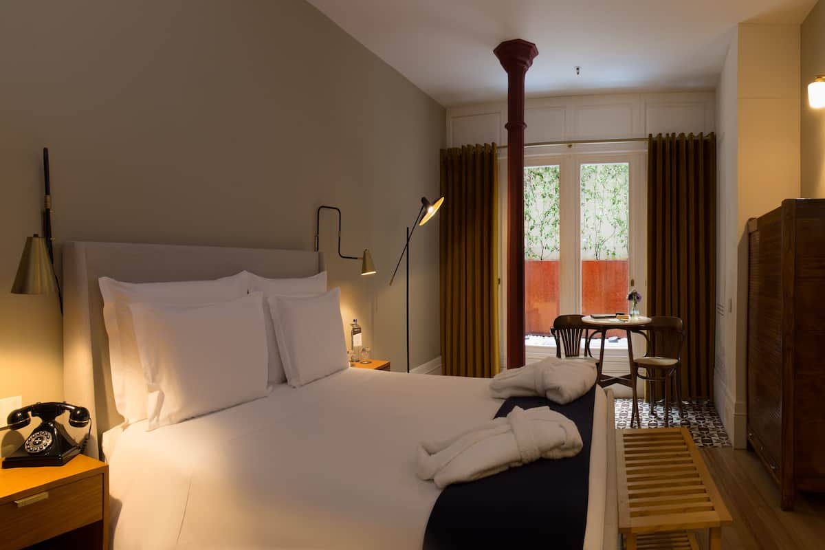 A hotel room with a bed, bedside lamp, telephone, and a window with curtains.