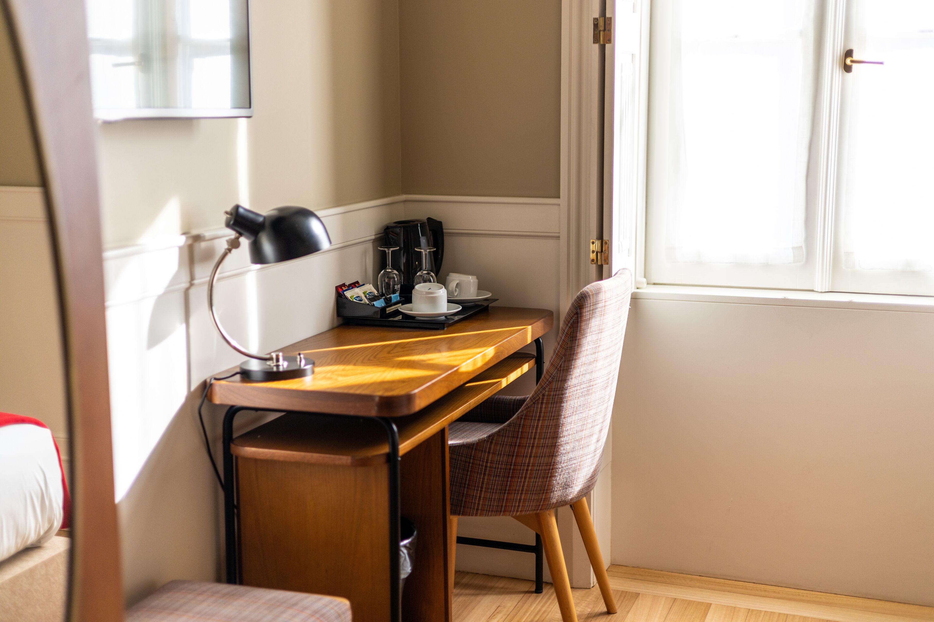 Une pièce de taille modeste, comprenant un bureau en bois, une chaise, une machine à café et une petite table avec des tasses et des verres.