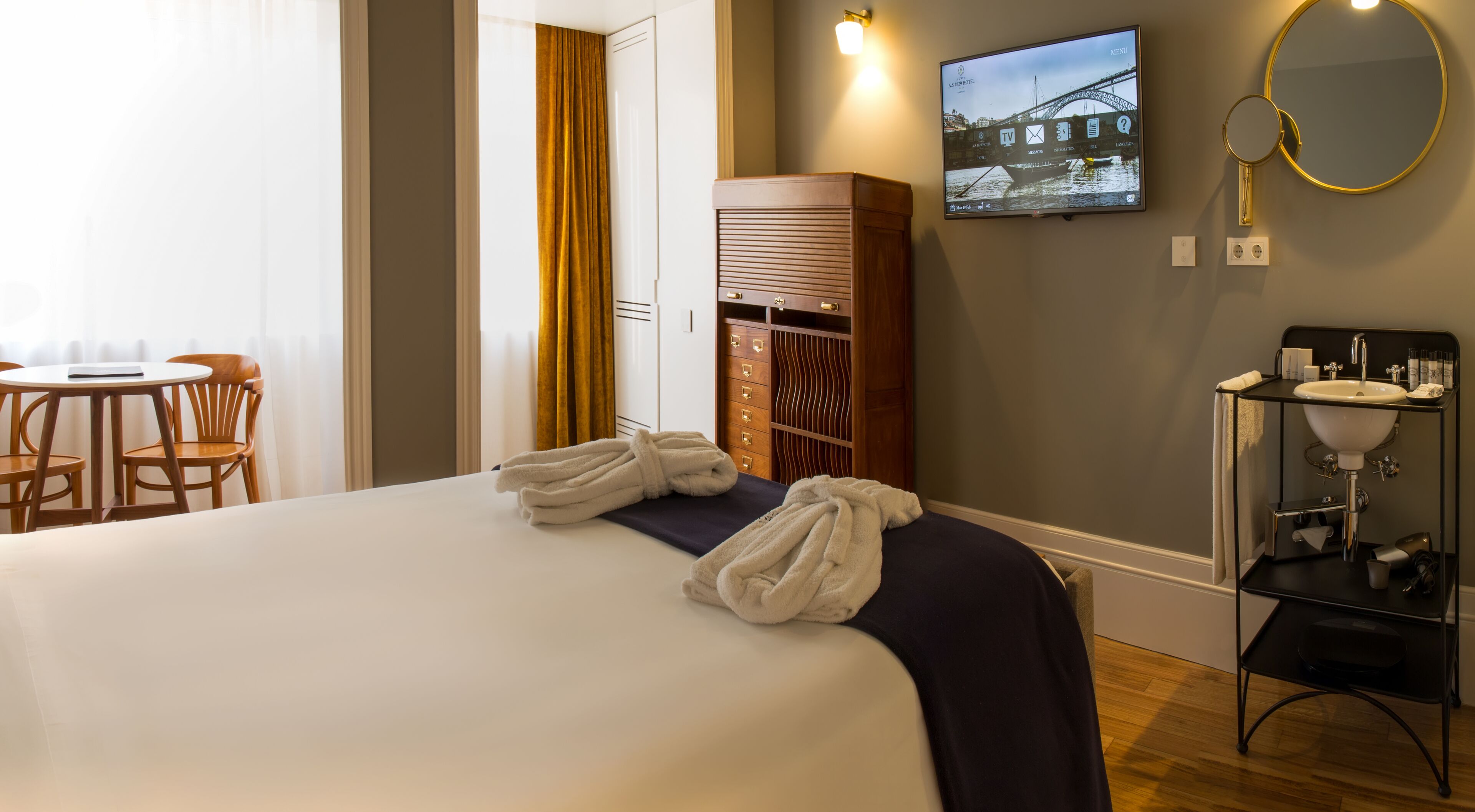 Une chambre d’hôtel comprenant un lit, un bureau avec des chaises, une armoire, une télévision et une salle de bain avec un lavabo et un miroir.
