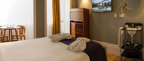Une chambre d’hôtel comprenant un lit, un bureau avec des chaises, une armoire, une télévision et une salle de bain avec un lavabo et un miroir.