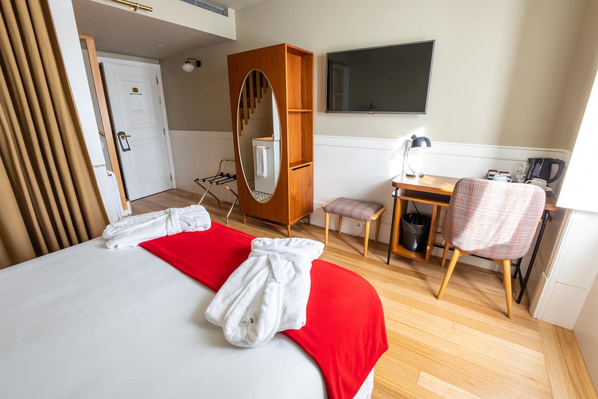 A hotel room with a bed, a desk, a chair, a TV, and a mirror.
