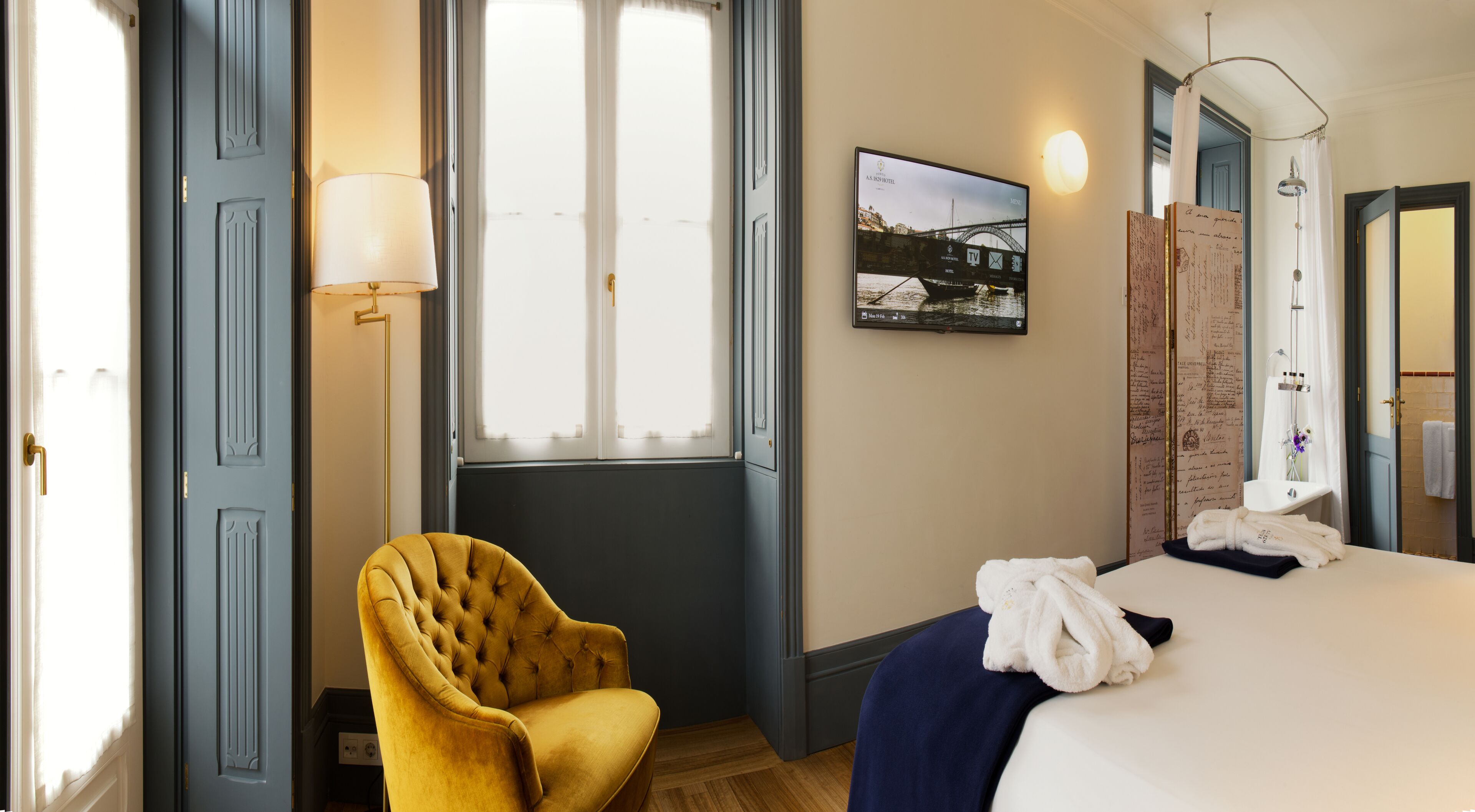 A hotel room with a bed, a chair, a TV, and a window with curtains.