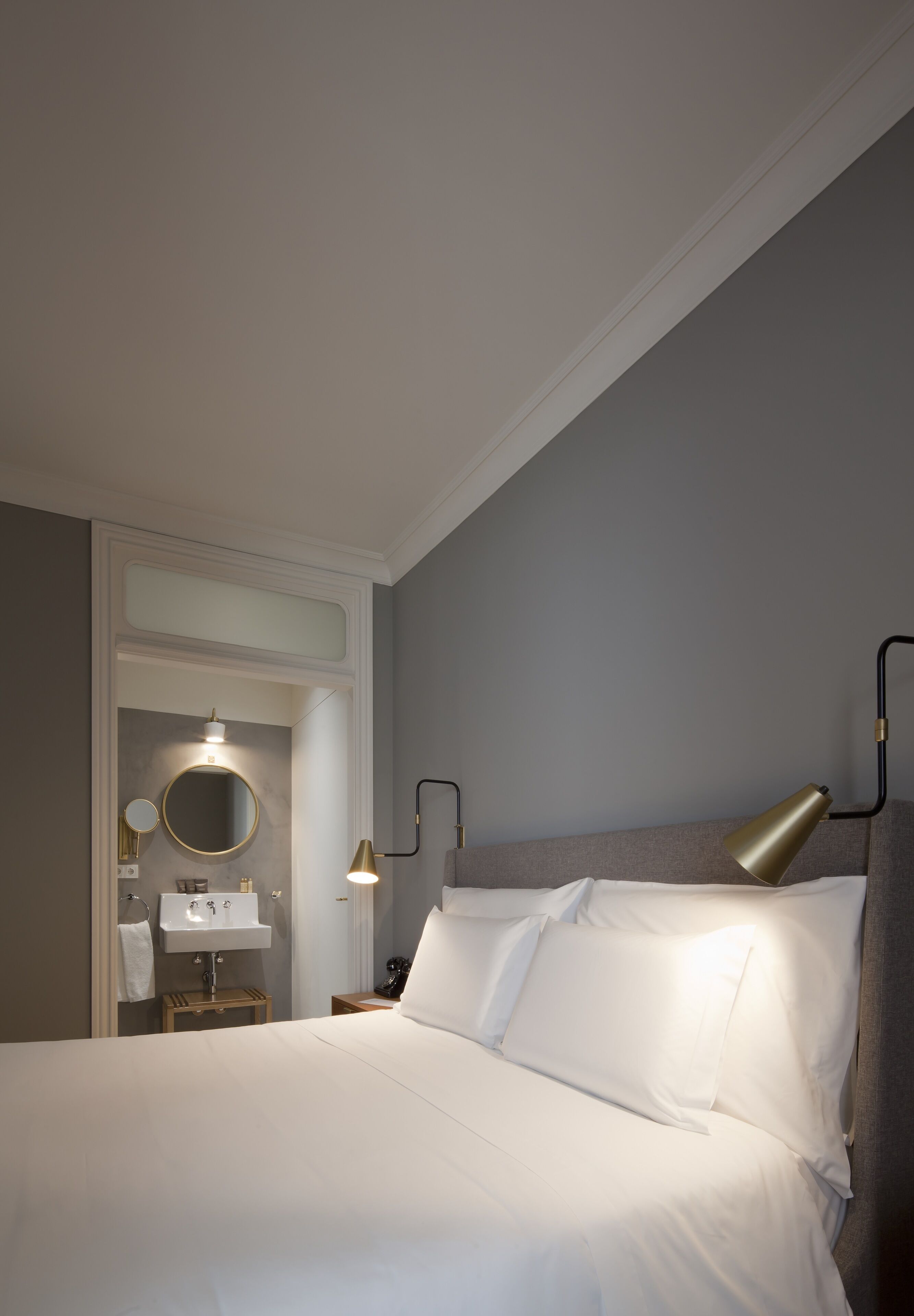 A neatly arranged hotel room with a bed, a bedside lamp, a mirror, and a small table with a lamp.