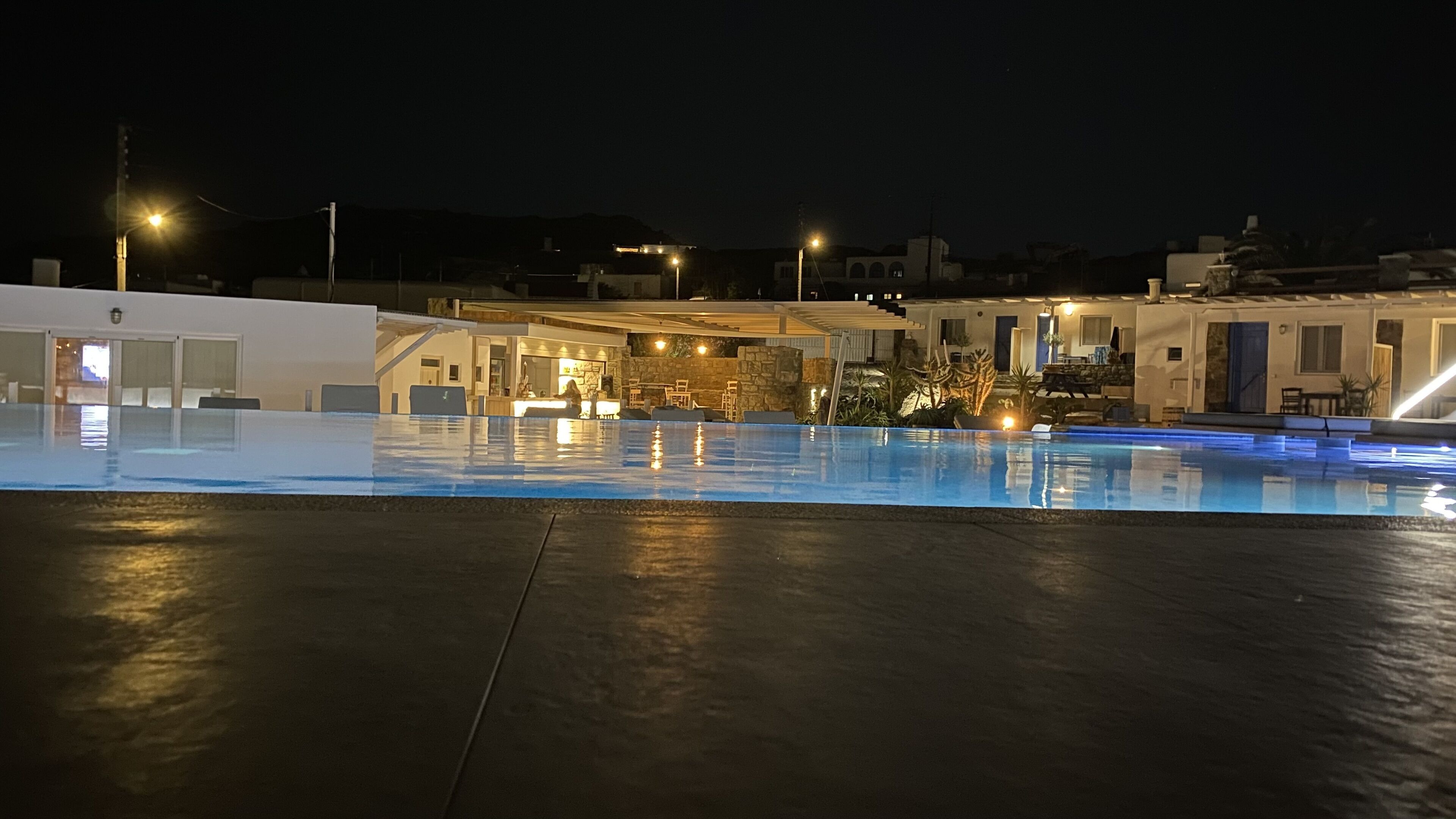 Una piscina con cubierta de piedra, mobiliario exterior e iluminada zona de patio.