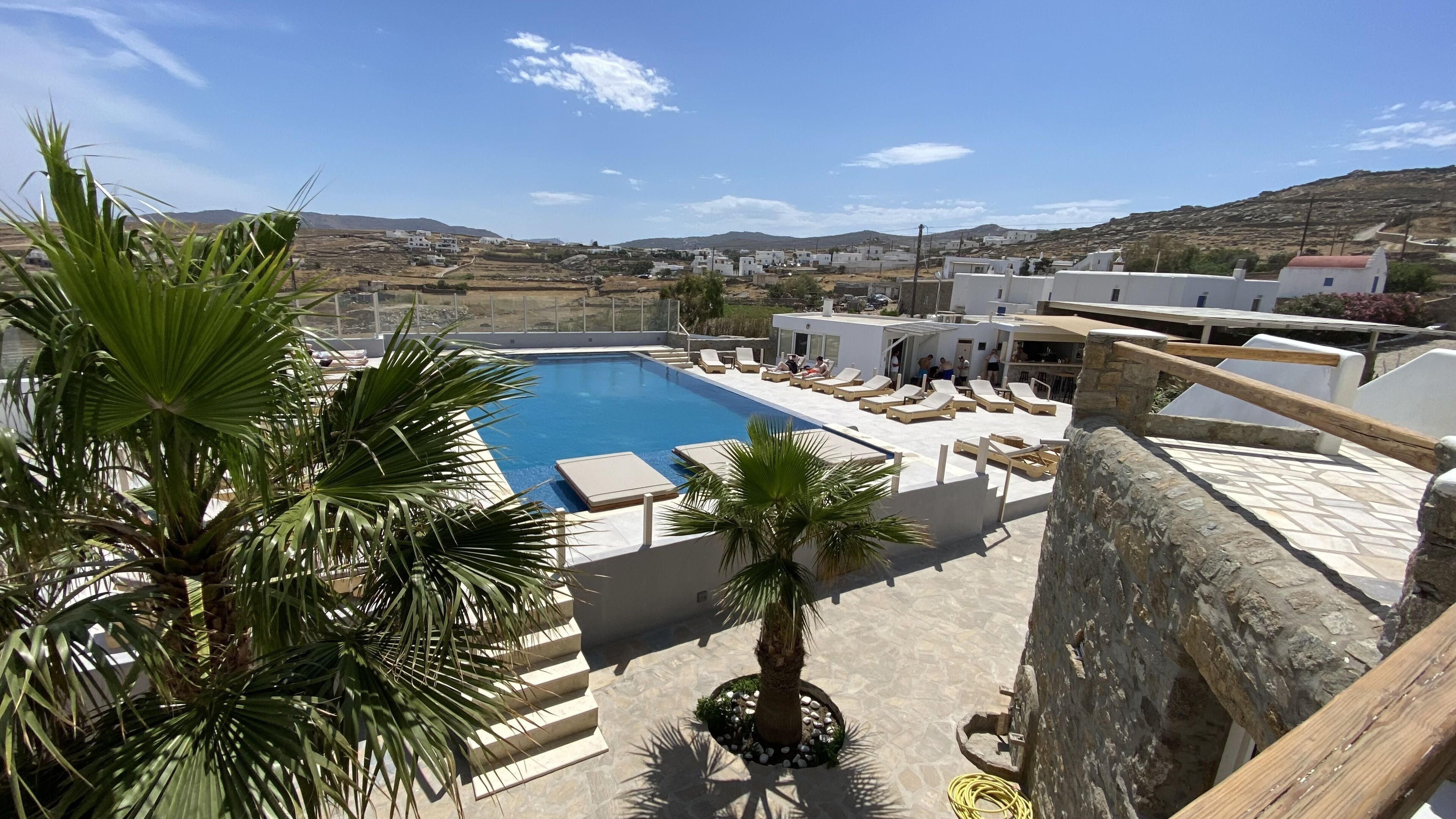 A pool area with lounge chairs, a palm tree, and a view of a hillside town.