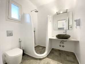 A modern bathroom with a curved shower, a toilet, a sink with a large mirror, and a hairdryer on the wall. - Alexandros Mykonos (Mykonos)