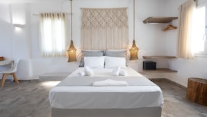 A modern bedroom with a large bed, bedside lamps, a macrame wall hanging, and a small wooden shelf. - Alexandros Mykonos (Mykonos)